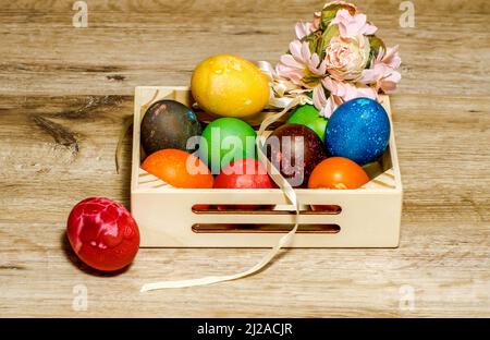 Osterkomposition, bunte, handbemalte Eier in einer kleinen Holzkiste angeordnet, Stillleben auf hellem Hintergrund, Blumen Stockfoto