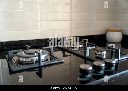Nahaufnahme eines modernen schwarzen Glasherds mit vier Brennern. Weiß geflieste Backsplash und Küchenzeile. Elegantes, minimalistisches Innendesign. Stockfoto