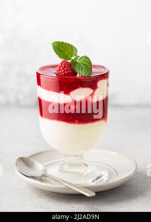 Ein Glas hausgemachtes Obst-Dessert mit Buttermilchcreme, Himbeersauce-Schichten und frischen Zitronenmelisse-Blättern garnieren. Stockfoto