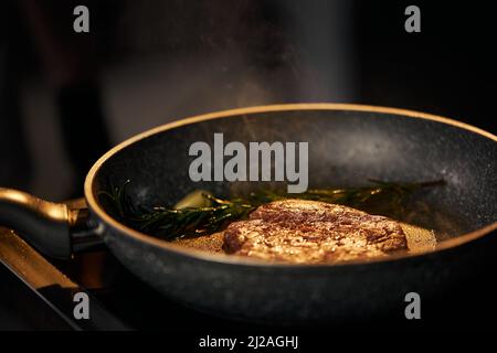 Nahaufnahme der Zubereitung appetitliches Rindfleisch-Burger auf dem Grill mit Kopierfläche. Braten und Rauchen saftiges Rindfleisch in der Pfanne mit Knoblauch und Rosmarinstick in der Restaurantküche . Konzept der Nahrung. Stockfoto