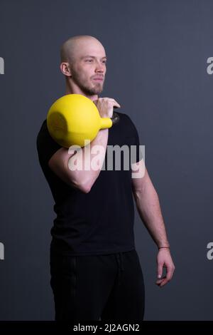 Kerl mit einer gelben Kettlebell-Fitnessstudio anonyme Trainingsstärke, am Nachmittag Motivation Bemühungen von Kommissionierung aus Gummi Jugend, südöstliche Aktivität Stockfoto