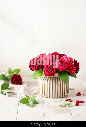 Schönes Bouquet von Sommer dunkelroten Rosen in Keramik Vase auf hellem Stein Mosaik Hintergrund. Floristisches oder Home-Deco-Konzept. Selektiver Fokus. Stockfoto