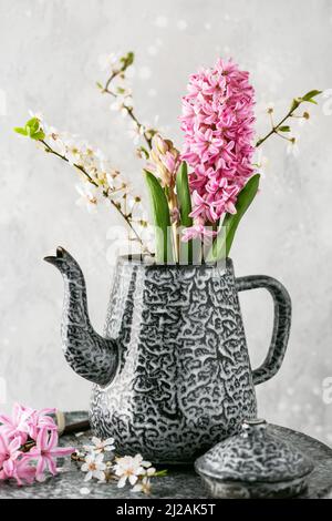 Wunderschöner Frühlingsstrauß aus rosa Hyazinthen und Pflaumenblütenzweigen in einer alten Emaille-Teekanne. Hausgemachte Osterdekoration. Stockfoto