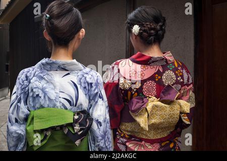 Horizontale Ansicht von zwei jungen Frauen mit dem Rücken, die traditionelle Yukatas in Gion, im südlichen Higashiyama-Distrikt, Kyoto, Japan, tragen Stockfoto