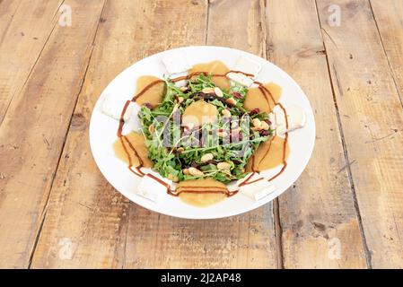 Salat mit Kürbiscreme, Rosinen, gebratenen Pinienkernen, Brie-Käse, Rucola und Balsamico-Essig Stockfoto