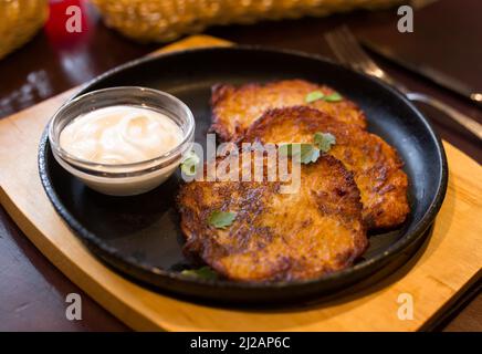 Weißrussische Küche. Appetitliche Kartoffeldraniki-Eintopf mit saurer Creme Stockfoto