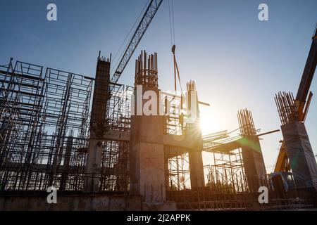 Silhouette einer großen Baustelle mit Kranen, die an einem Gebäudekomplex arbeiten, mit klarem blauen Himmel und der Sonne auf der Baustelle. Stockfoto