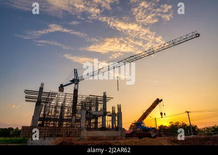 Silhouette der Baustelle mit Kranen, die an einem Gebäudekomplex arbeiten, mit klarem blauen Himmel und der Sonne auf der Baustelle. Stockfoto