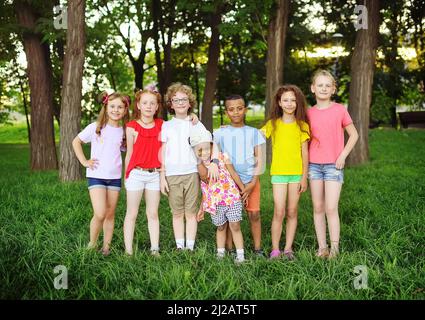 Eine Gruppe von Vorschulkinder verschiedener Rassen umarmen und lächeln vor dem Hintergrund von Grün und einem Park. Kinderschutztag. Stockfoto