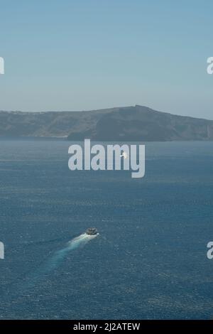 Blick auf ein kleines Fährschiff, das gerade den Hafen von Santorini verließ und Möwe darüber flog Stockfoto