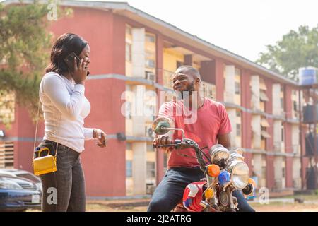 Eine Nahaufnahme einer Afrikanerin, die am Telefon neben dem Motorradfahrer steht. Stockfoto