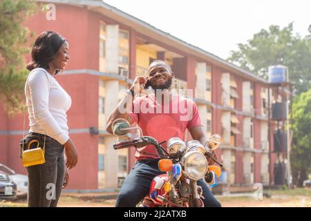 Eine Nahaufnahme eines afrikanischen Mannes auf dem Fahrrad, der am Telefon sprach, während die Frau neben ihm stand. Stockfoto
