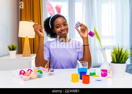 afroamerikanische Frau in rosa Hasenohren, die Eier für den ostertag malt Stockfoto