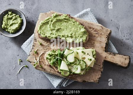 Blick von oben auf appetitliche Toast mit Guacamole und Gurken und Käse auf rustikalem Holzbrett auf Betontisch serviert Stockfoto