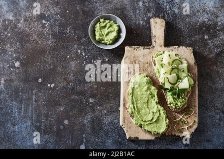 Von oben appetitlich Toast mit Guacamole und Käse und Gurken auf Holz Schneidebrett für vegetarisches Frühstück gelegt Stockfoto