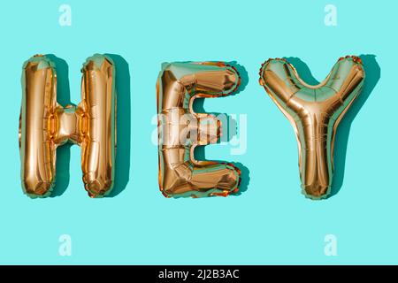 goldene, buchstabenförmige Luftballons bilden das Wort hey auf blauem Hintergrund Stockfoto