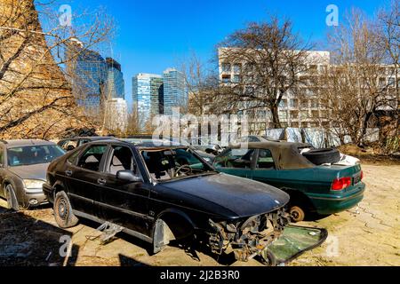 Warschau, Polen - 18. März 2022: Wrackwagen-Schrottplatz mit Wolkenkratzern des modernen Wola-Geschäftsviertels von Warschau im Hintergrund Stockfoto