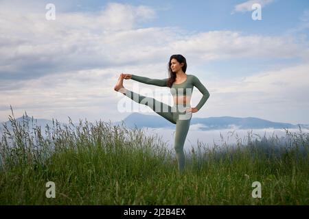 Junge sportliche Frau mit aktivem Outfit, die im Stretching-Training in den Sommerbergen trainiert. Morgens Zeit für aktives Training. Gesunde Lebensweise. Stockfoto