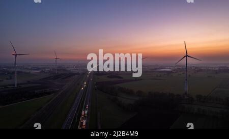 Luftaufnahme Sonnenaufgang von Wiesen und elektrischen Windmühlen über Hochgeschwindigkeitsautobahn am Morgen unter einem bunten Himmel natürliche Landschaft über der Panoramalandschaft. Hochwertige Fotos Stockfoto