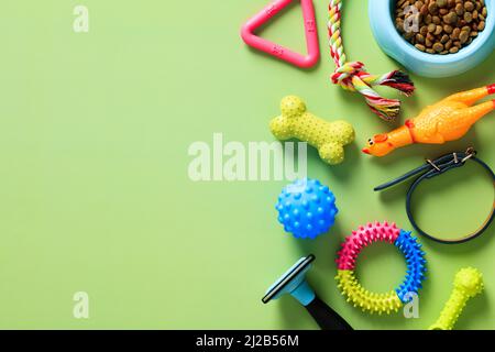 Haustierspielzeug für Training, Pflegeausrüstung und Schale mit Trockenfutter auf grünem Hintergrund. Draufsicht mit Kopierbereich. Flach liegend. Stockfoto