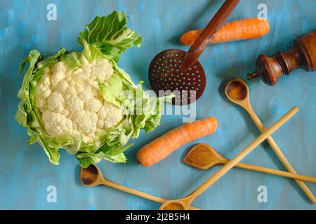 Flaches Lay mit frischem Blumenkohl, Holzlöffeln und Karotten.gesundes Essen, Diät, veganes Lebensmittelkonzept. Stockfoto