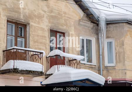 Scharfe Eiszapfen hängen am Abflussrohr am Rand des Dachs. Vor dem Hintergrund der Mauer eines alten Backsteinhauses. Große Kaskaden, sogar schöne Reihen. Wolkiger Wintertag, weiches Licht. Stockfoto