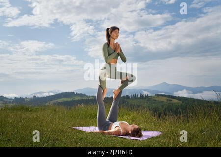 Zwei sportliche junge Frauen im aktiven Ohr verbringen Zeit im Freien für akrobatische Yoga-Übungen. Konzept von Menschen, aktiven Lebensstilen und Wohlbefinden. Stockfoto