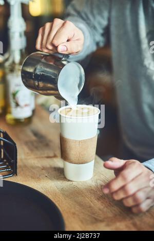 Mischen auf einer Tasse Magie. Nahaufnahme eines unerkennbaren Barista, der in einem Café Milch in eine Tasse frisch gebrühten Kaffee gießt. Stockfoto