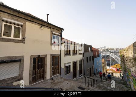 Porto, Portugal. 2022. März. Eine typische Straße zwischen den alten Häusern der Innenstadt, die mit der Eisenbride Dom Luís i zum Fluss hinunter geht Stockfoto