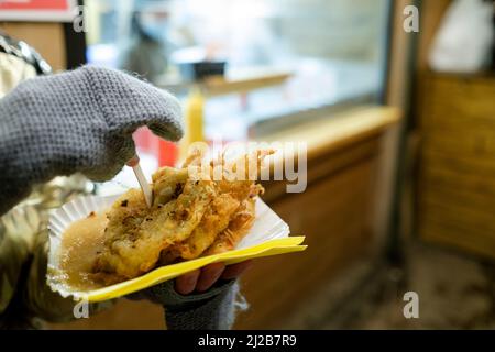 Deutschland, Aachen (Aix-la-Chapelle), 21. Dezember 2021: Weihnachtsmarkt. Frau beim Essen eines Reibekuchen oder Kartoffelpuffers, einer traditionellen deutschen Kartoffelpanca Stockfoto
