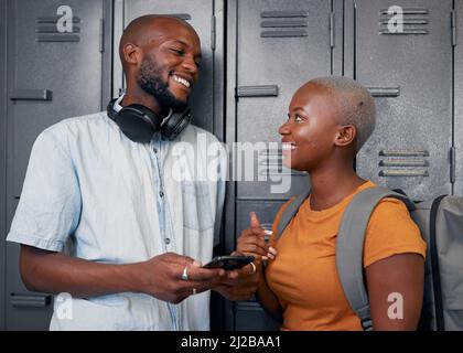 Zwei schwarze Schüler lachen und plaudern mit dem Handy vor den Schließfächern der Schule Stockfoto