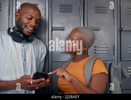 Zwei schwarze Schüler lachen und plaudern mit dem Handy vor den Schließfächern der Schule Stockfoto