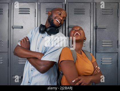 Zwei junge schwarze Studenten lachen und posieren vor den Schließfächern des Campus in der Schule Stockfoto