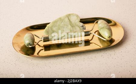 Gua Sha Massage Steininstrumente. Abstreifer und Walze auf dem Ständer. Konzept der Gesichts- und Hautpflege. Lifting und Anti-Age-Behandlung. Kosmetischer Naturtrend. Hochwertige Fotos Stockfoto