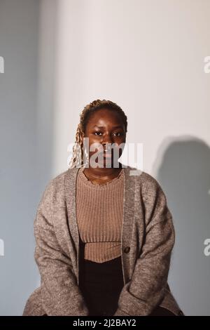 Porträt einer jungen Frau, die im Studio vor weißem Hintergrund sitzt Stockfoto
