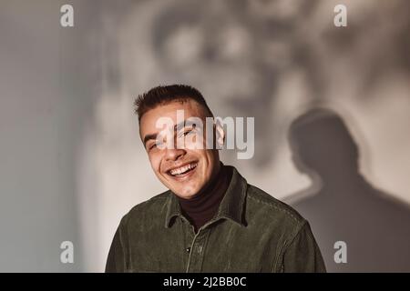 Porträt eines jungen Mannes, der vor weißem Hintergrund lacht Stockfoto