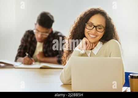 Konzentriert sich auf ihre Studien. Eine kurze Aufnahme einer attraktiven jungen College-Studentin, die während des Unterrichts an ihrem Laptop arbeitet. Stockfoto