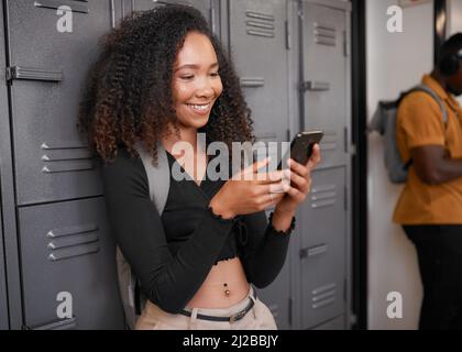 Eine junge Frau mit gemischter Rasse lächelt und SMS an Freunde am College Stockfoto