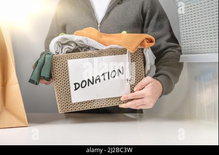 Spendenkonzept. Spendenbox mit Spendenkleidung. Hilfe für arme und bedürftige Menschen. Spendenbox für Arme mit Kleidung in männlichen Händen. Mann mit einem Stockfoto