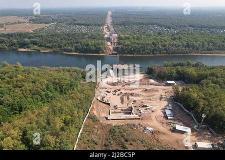 Draufsicht auf den Bau einer Brücke über den Fluss. Luftaufnahmen von einer Drohne auf einer Baustelle, Sonderausrüstung und Arbeiter, sowie Stockfoto