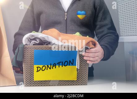 Sammelt Kleiderspenden für ukrainische Flüchtlinge, Unterstützung für die ukraine, humanitäre Hilfe. Box mit Spenden Kleidung für ukrainische Flüchtlinge leiden f Stockfoto