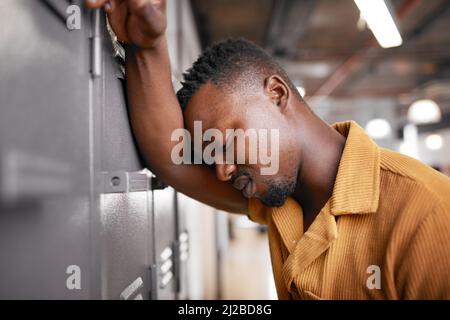 Ein junger schwarzer Mann lehnt sich an die Umkleide des Campus und schaut aufgeregt auf die Hochschule Stockfoto