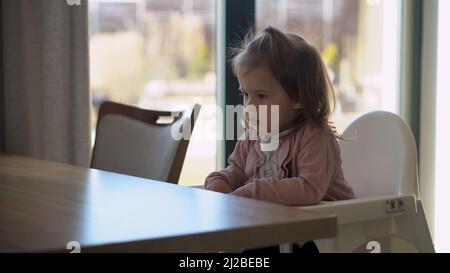 Nahaufnahme von jungen Baby in weiß Fütterung Hochstuhl, Kind versucht, sich selbst zu essen, glückliches Kind mit Essen verschmutztes Gesicht, kleines Mädchen isst Brei mit Stockfoto