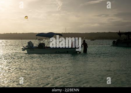 San Andrés, Kolumbien - 18 2021. November: Weißes und blaues Boot mit Motor an Shore gebunden, zwei Männer sprechen bei Sonnenuntergang Stockfoto