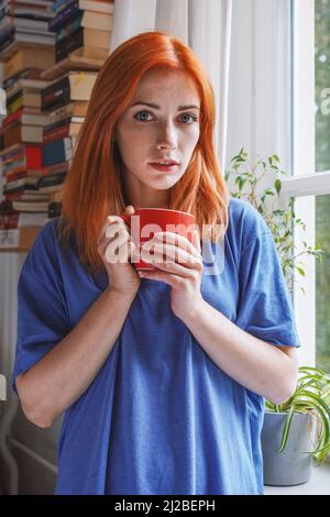 Junge Frau, die zu Hause in ihrem Wohnzimmer mit einer Kaffeetasse steht Stockfoto