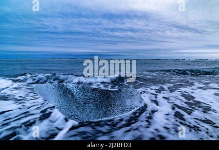 Kleine Eisblöcke und ankommende Wellen am Diamond Beach mit schwarzem Sand, Breidamerkursandur, Island Stockfoto
