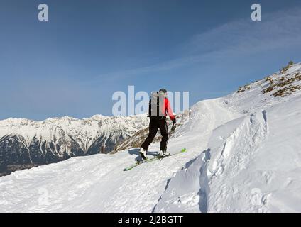 Generisches Bild eines Mannes mit Rucksack und Stöcken, der mit Skiern einen verschneiten Berg gegen einen blauen Himmel hinaufgeht (Patscherkofel, Alpen, Österreich) Stockfoto