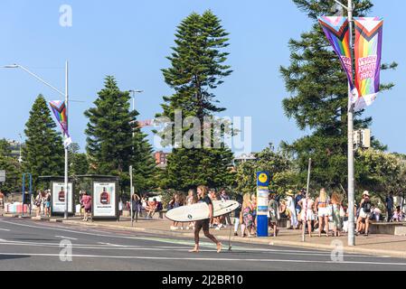 Ein Surfer mit seinem Surfbrett, als er die Campbell Parade am Bondi Beach überquert Stockfoto