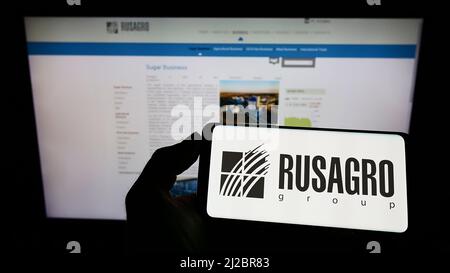 Person, die Mobiltelefon mit Logo der russischen landwirtschaftlichen Firma Rusagro Group auf dem Bildschirm vor der Business-Webseite hält. Konzentrieren Sie sich auf die Telefonanzeige. Stockfoto