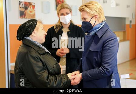 Schwerin, Deutschland. 31. März 2022. Nina (66) (l-r) aus der Ukraine und Manuela Schwesig (SPD), Ministerpräsidentin von Mecklenburg-Vorpommern, sagen Auf Wiedersehen im Speisesaal des AWO-Feriendorfes Muess, im Hintergrund Donata Wustlich, Dolmetscherin. Bei ihrem Besuch bei den ukrainischen Flüchtlingen erfuhr Schwesig von der Situation im Feriendorf. Quelle: Bernd Wüstneck/dpa-Zentralbild/dpa/Alamy Live News Stockfoto